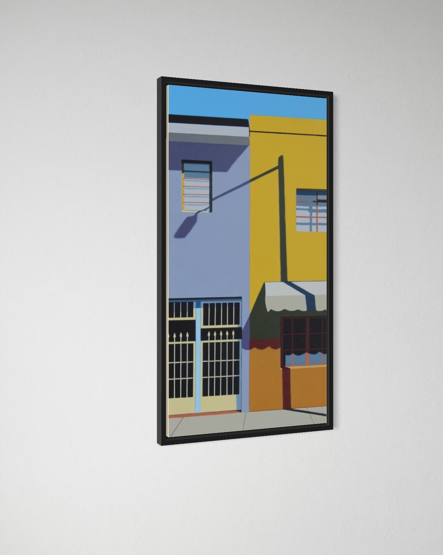 Framed artwork of a colorful street scene with buildings on a white wall