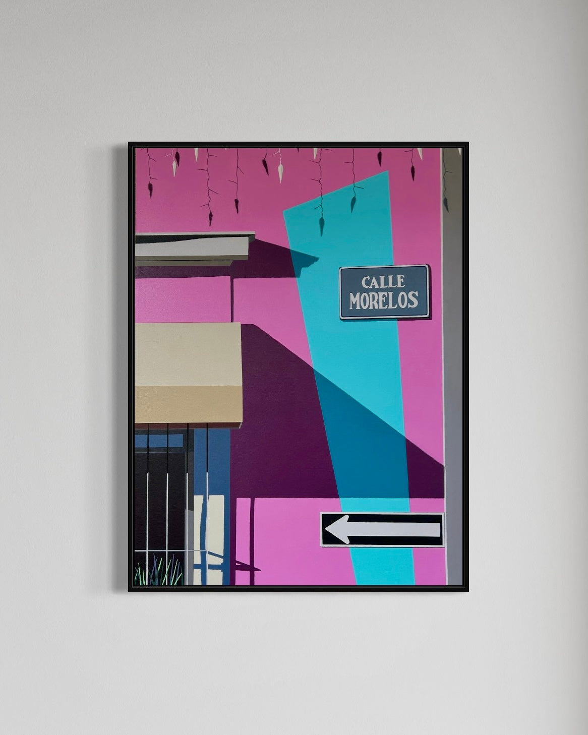 Framed colorful artwork with geometric shapes and a street sign on a gray wall.